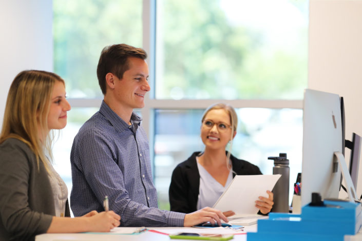 three employees collaborating at standing desk at bright age social media agency