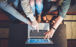 Three girls pointing at laptop showing social media brand awareness